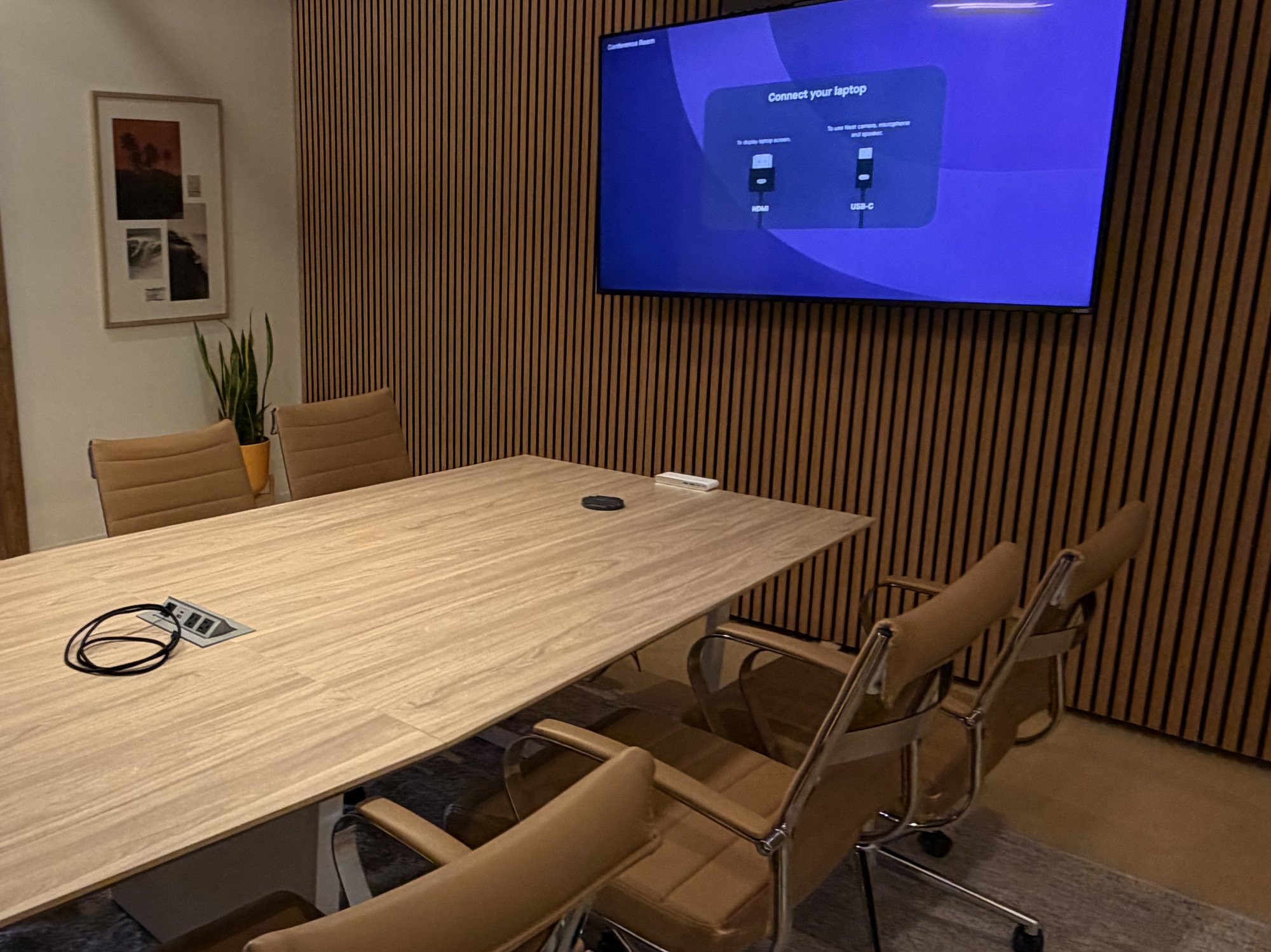 The Conference Room&rsquo;s 4K TV on the wood slat wall above the meeting table, showing its HDMI and USB-C connection screen
